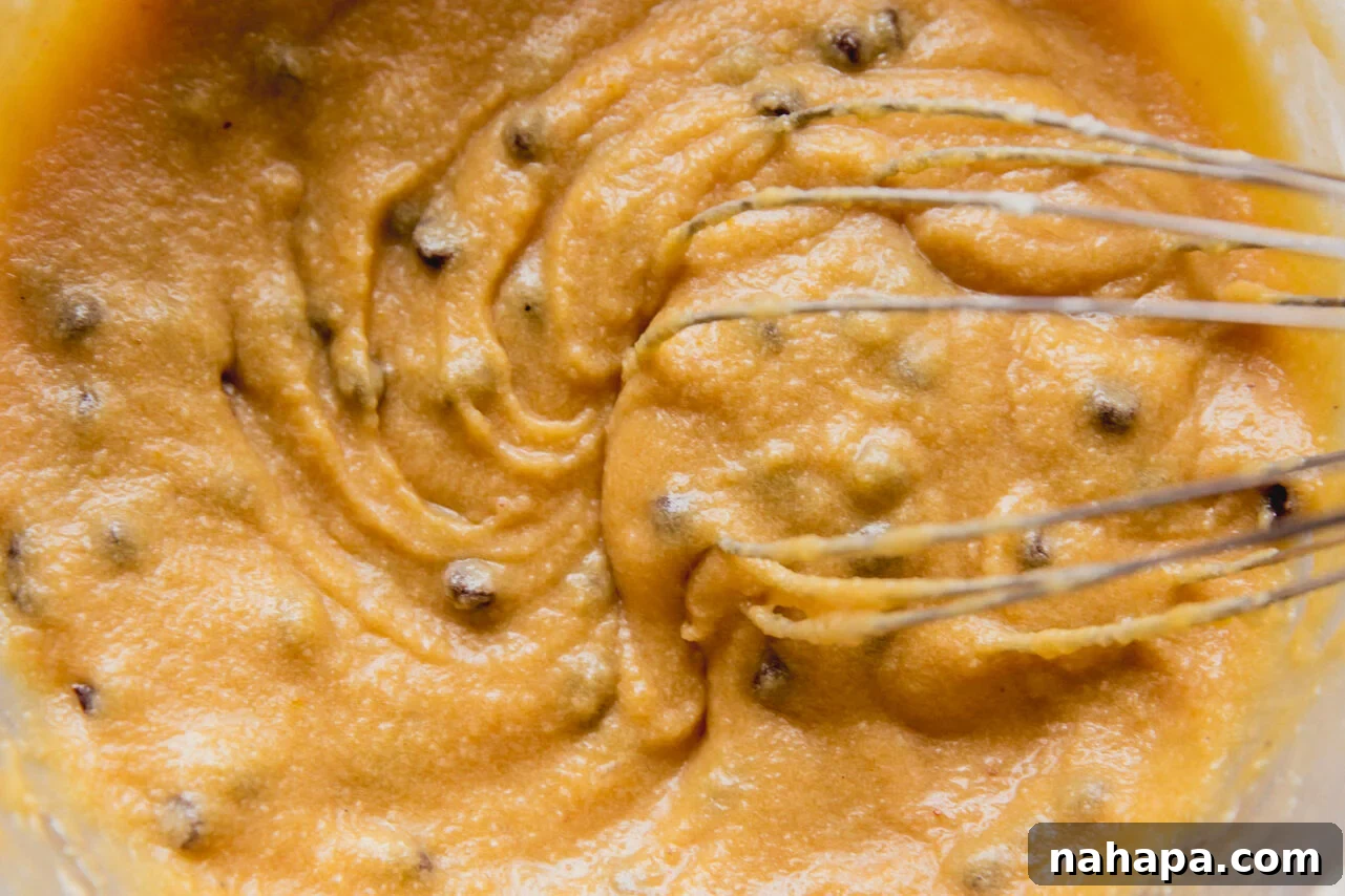 Decadent Gluten-Free Chocolate Chip Cookie Pie 5 A rich chocolate chip cookie pie filling being whisked in a large glass bowl, showcasing its smooth texture and scattered chocolate chips.