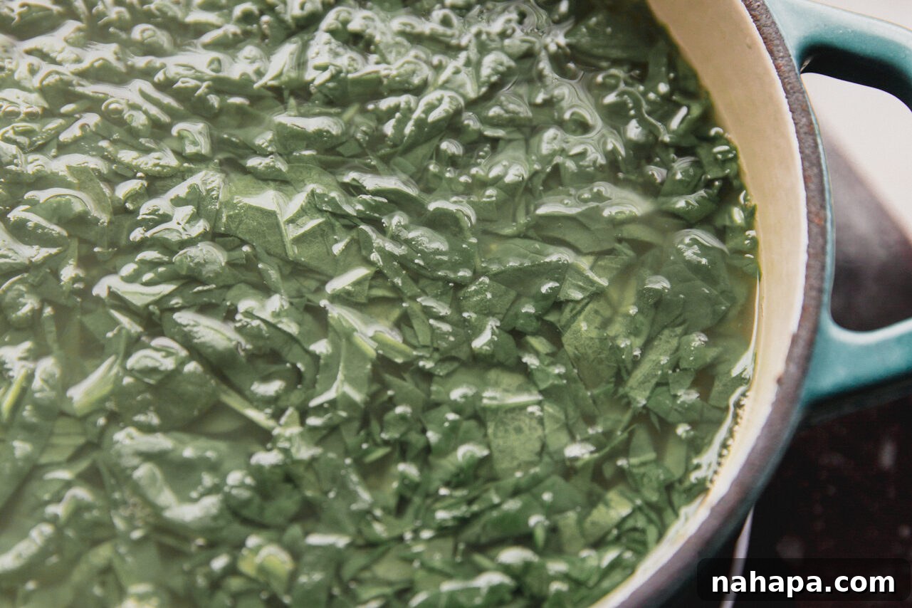 Chicken broth, lemon juice, and spinach simmering gently in a large pot on the stovetop.