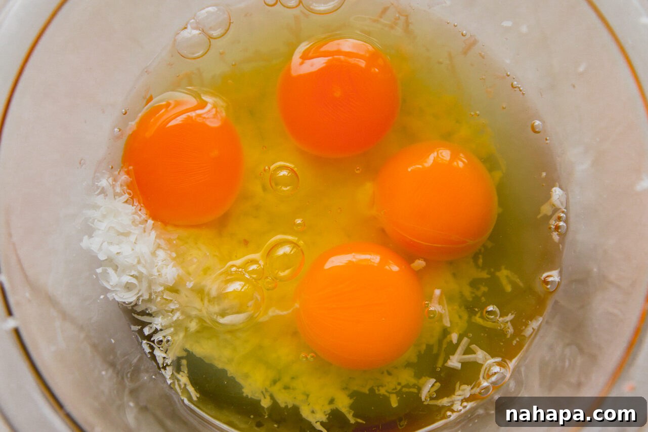 A glass bowl containing four raw eggs and grated cheese, ready for mixing.