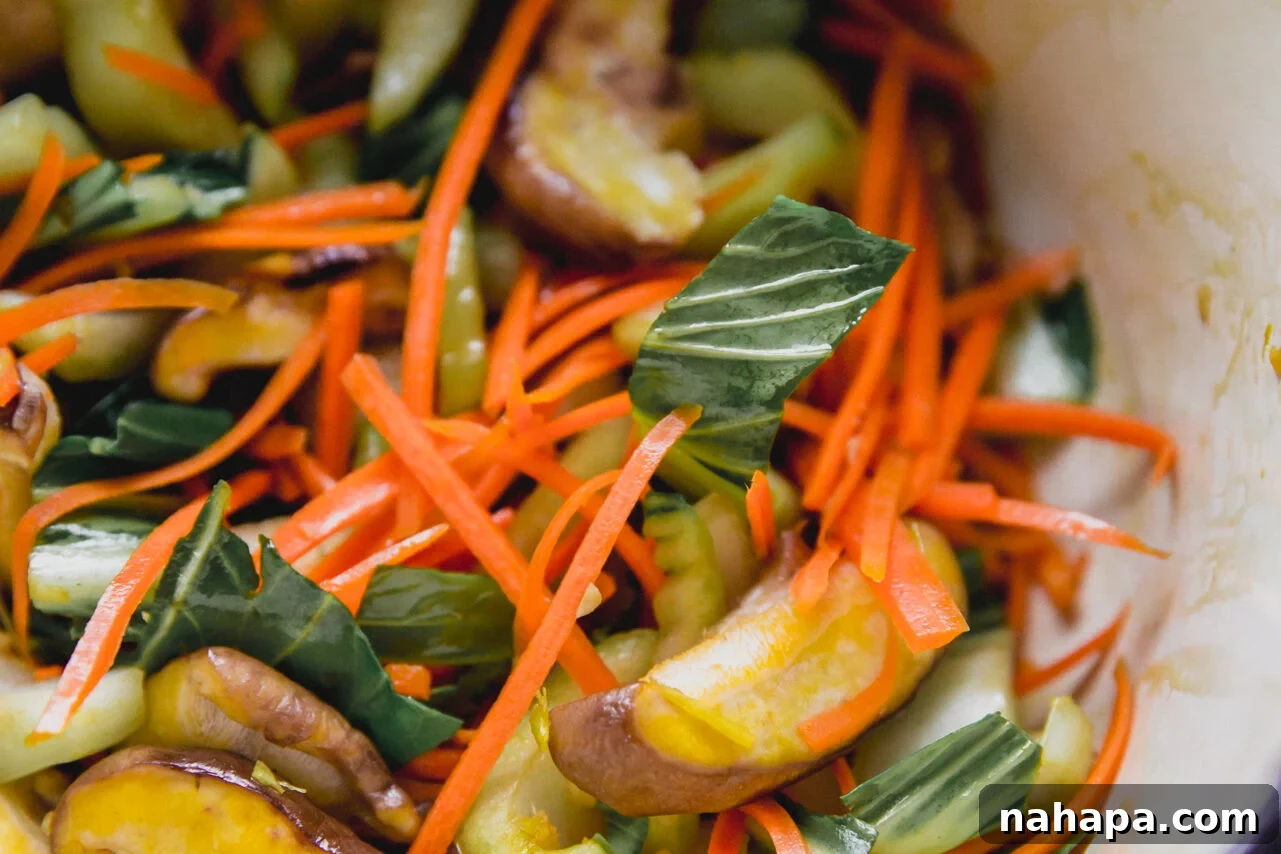 A close-up view of minced garlic, ginger, bok choy, and carrots sautéing in a pan, releasing their fragrant aromas.