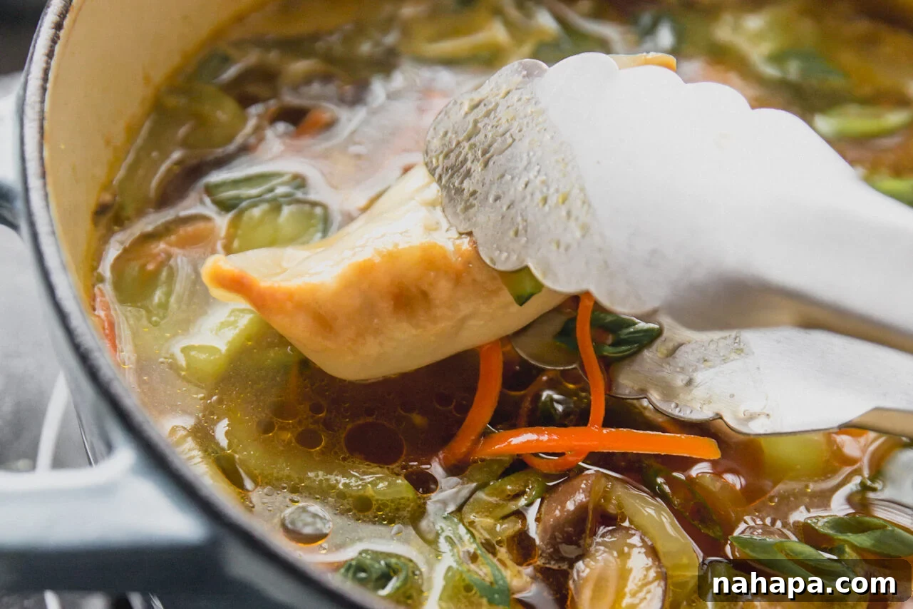 Metal tongs gently placing a cooked potsticker into a simmering pot of soup with vegetables, creating a vibrant scene on the stove.