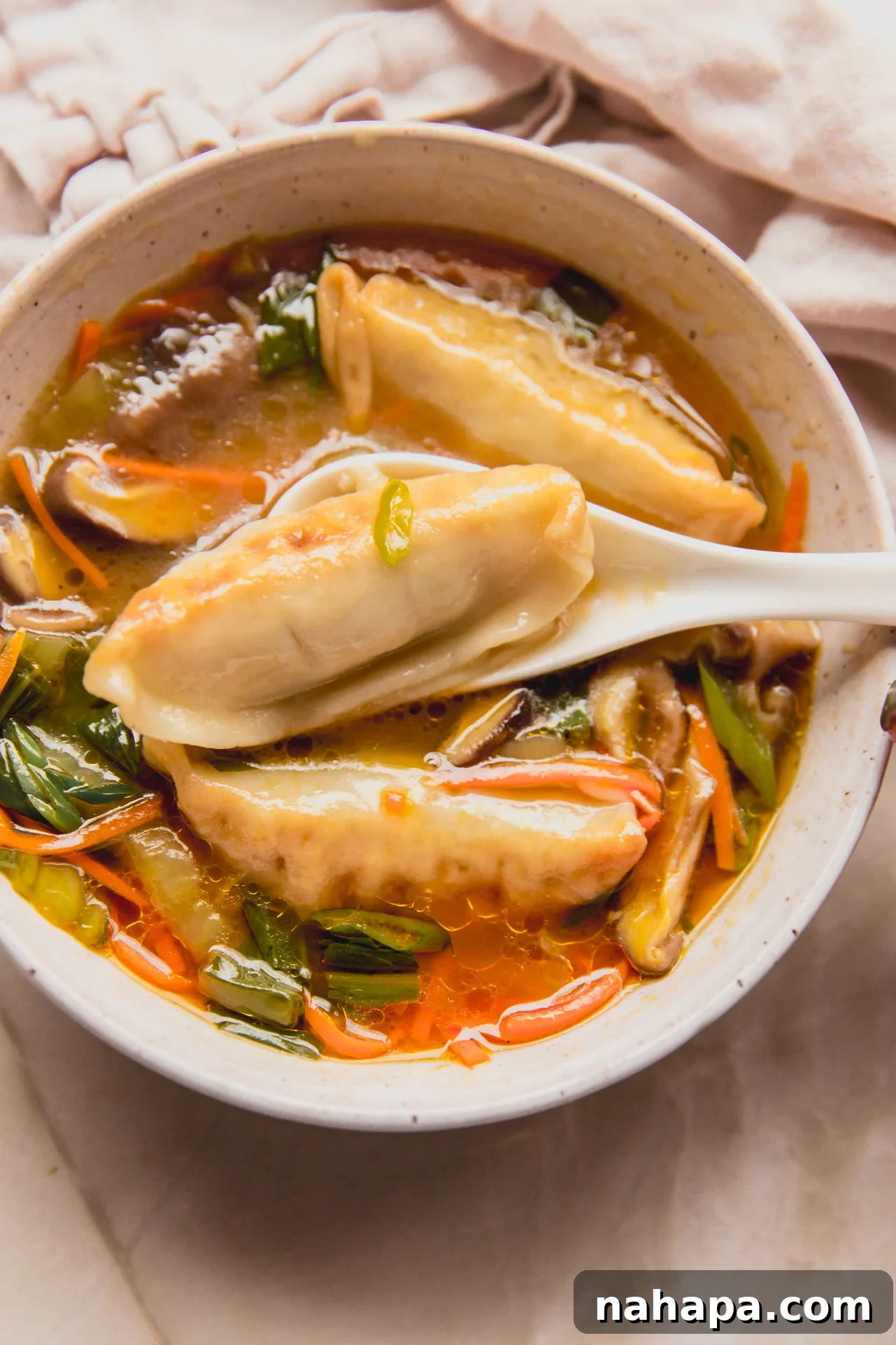 Gluten free potsticker soup in a bowl with a spoon scooping a potsticker out.