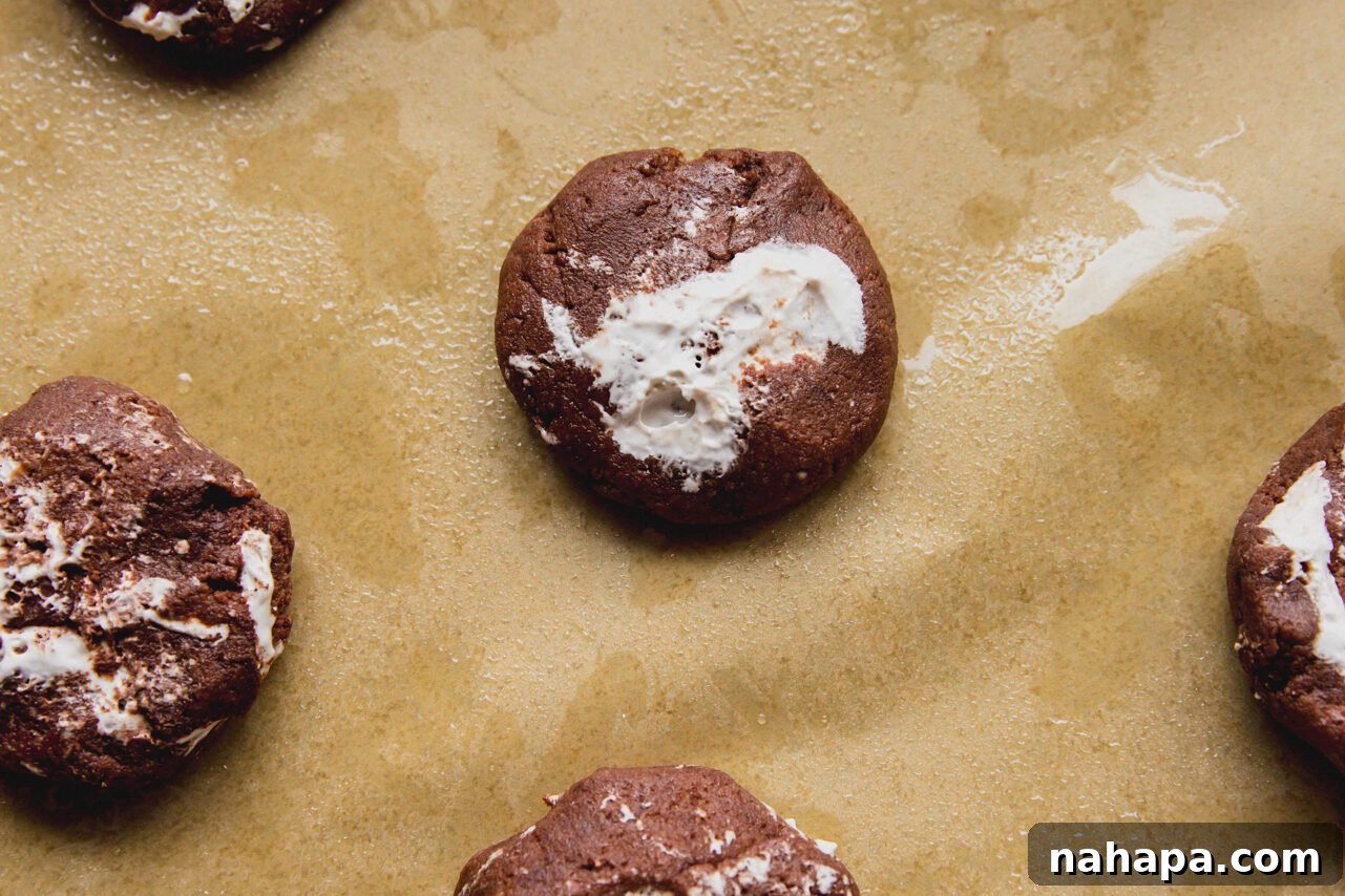Six perfectly baked chocolate marshmallow fluff cookies cooling on parchment paper after being removed from the oven.