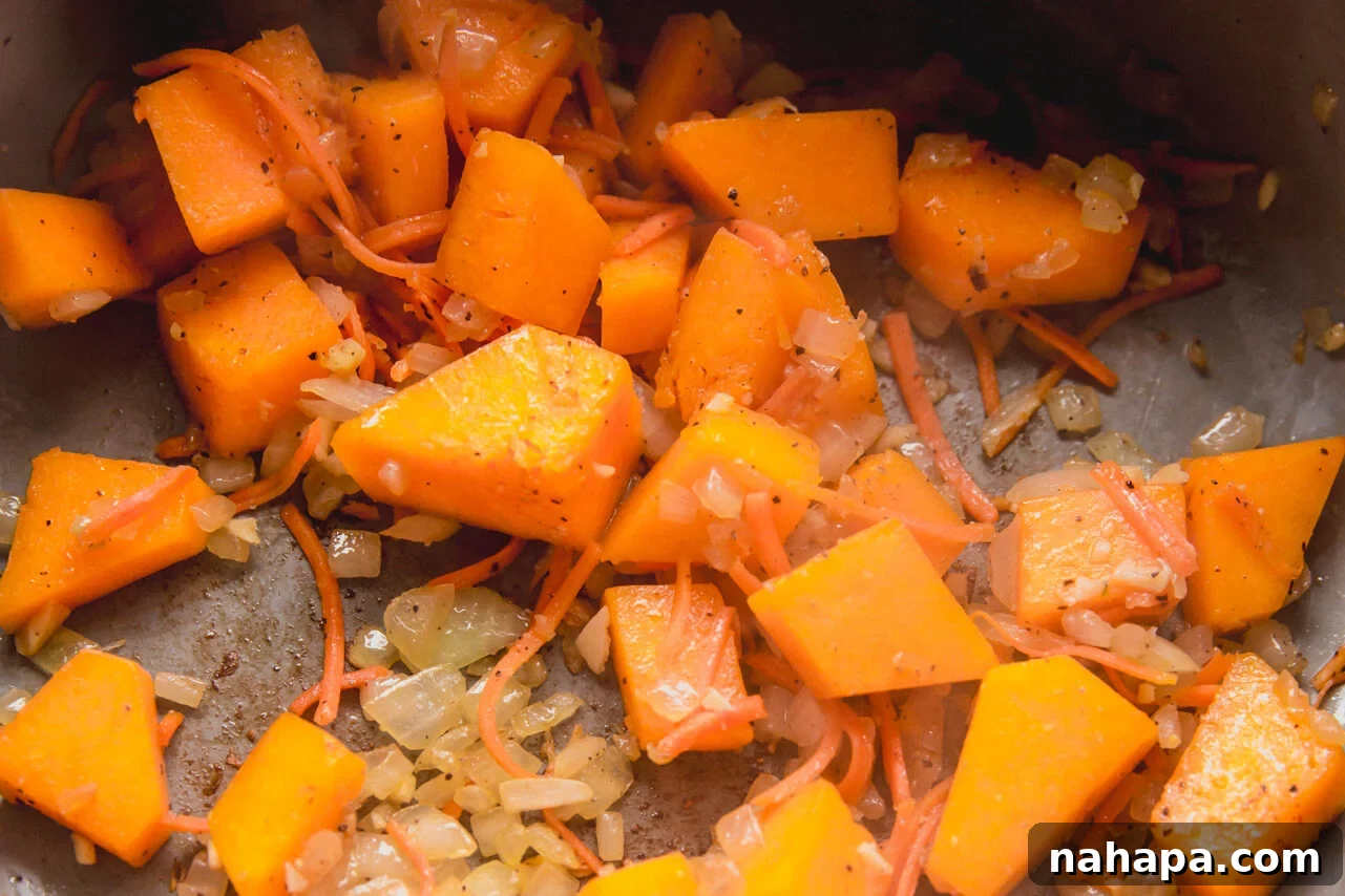 Sautéing diced onion, garlic, cubed butternut squash, and shredded carrots in a pot with avocado oil.