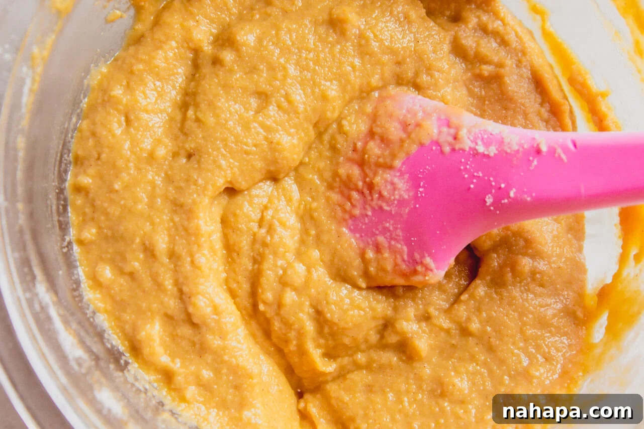 A glass bowl filled with cinnamon roll cake batter and a pink spatula.