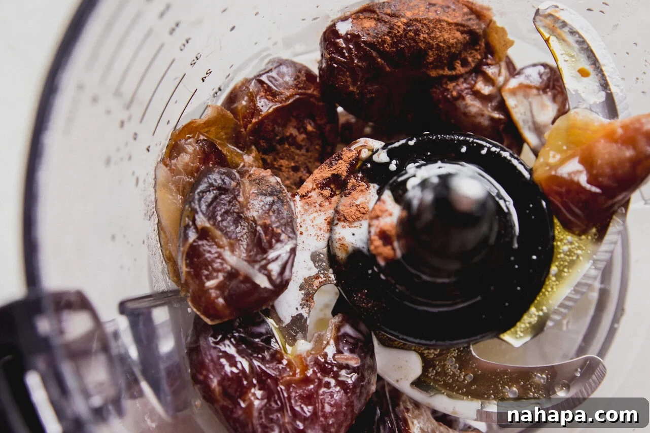 A food processor blending dates, coconut oil, ghee, and cinnamon.
