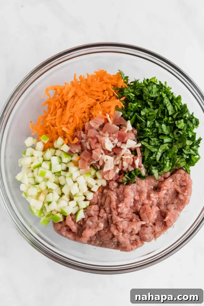Bowl filled with raw ingredients for chicken sausage including ground chicken, shredded sweet potato, and spinach