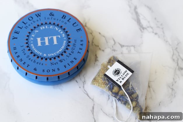 YBC Mantra Box Summer 2017 Unveiled Natural Paleo and Yoga Essentials 3 An elegantly designed tin of Harney & Sons fine tea blend, accompanied by a single delicate tea bag, presented on a clean surface, emphasizing its sophisticated packaging and inviting appeal.