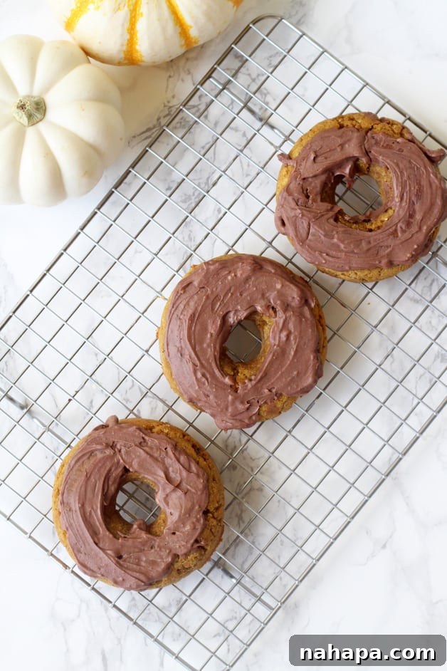 Three pumpkin donuts frosted sitting on a metal cooling rack.