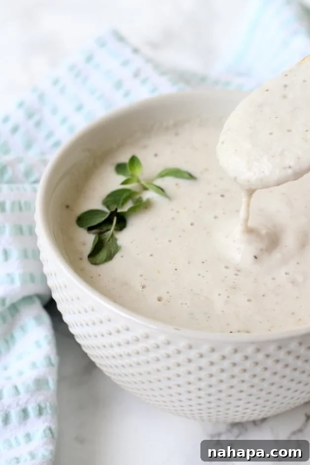 Indulgent Oregano Garlic Cream Sauce Whole30 Paleo AIP 2 A bowl of garlic cream sauce with a spoon taking a spoonful out, highlighting its creamy texture and rich consistency.