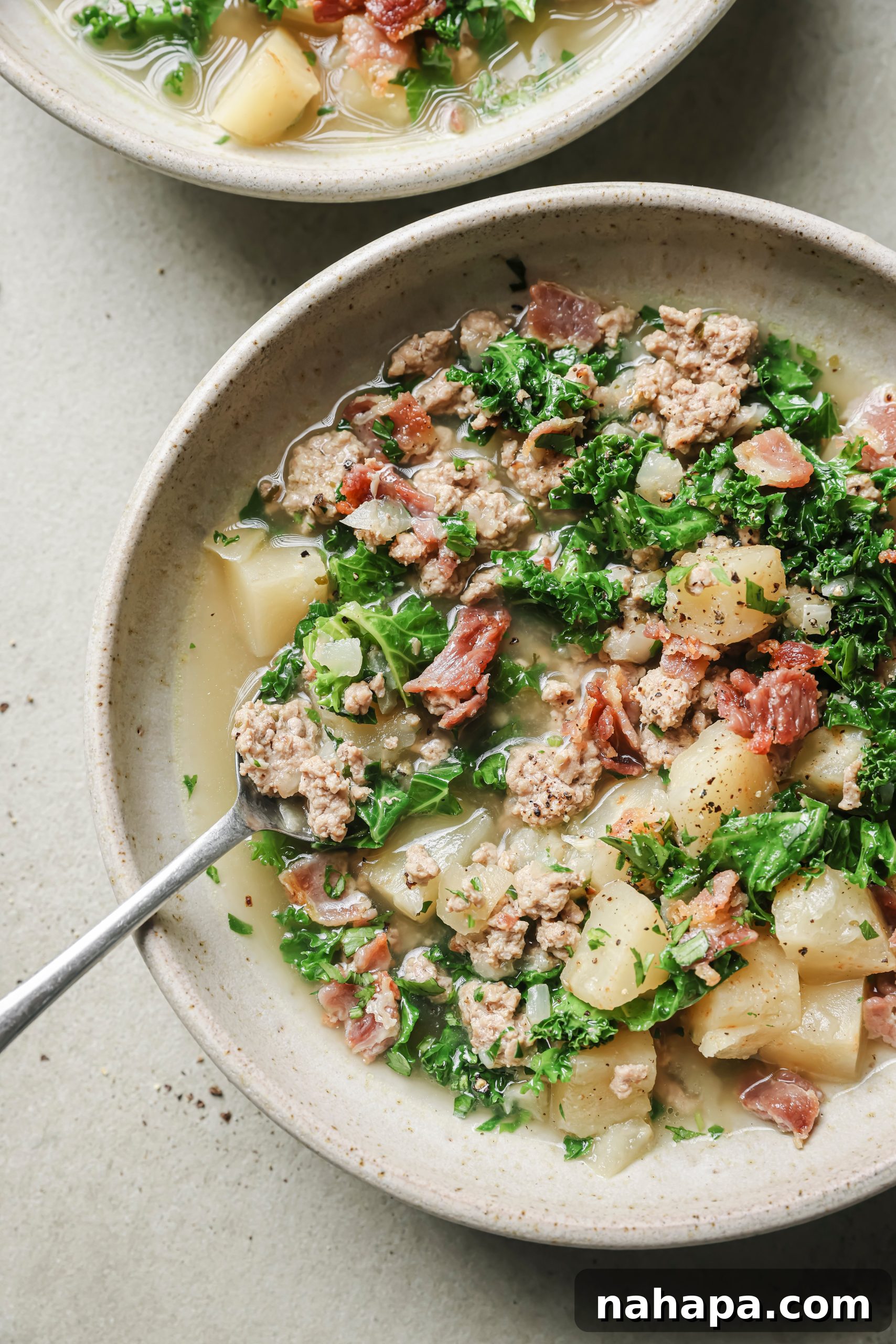 A steaming bowl of Instant Pot Zuppa Toscana soup with a spoon, garnished with bacon and parsley.