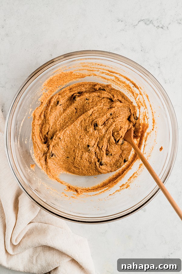 A bowl of pumpkin chocolate chip cookie skillet dough being mixed with a wooden spoon, showcasing its thick, rich texture before baking.