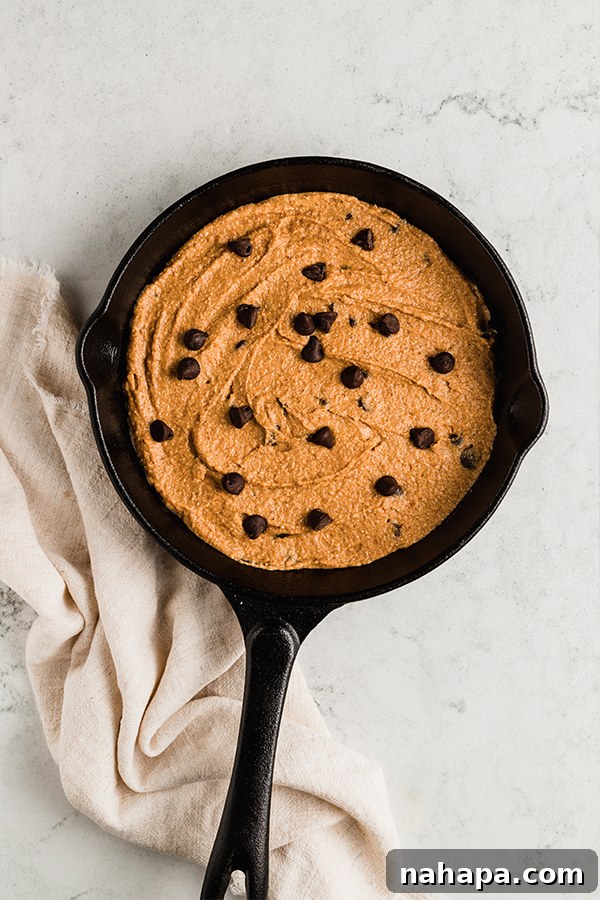 A cast iron skillet filled with smooth pumpkin chocolate chip cookie dough, ready to be baked into a warm and comforting dessert.