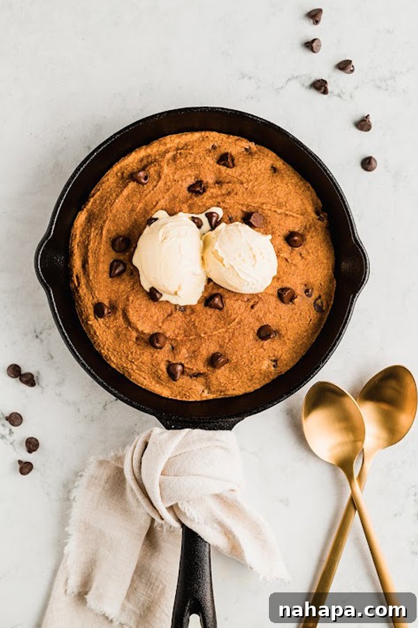 The warm, gooey pumpkin chocolate chip cookie skillet generously topped with melting coconut milk ice cream, a perfect sweet treat.