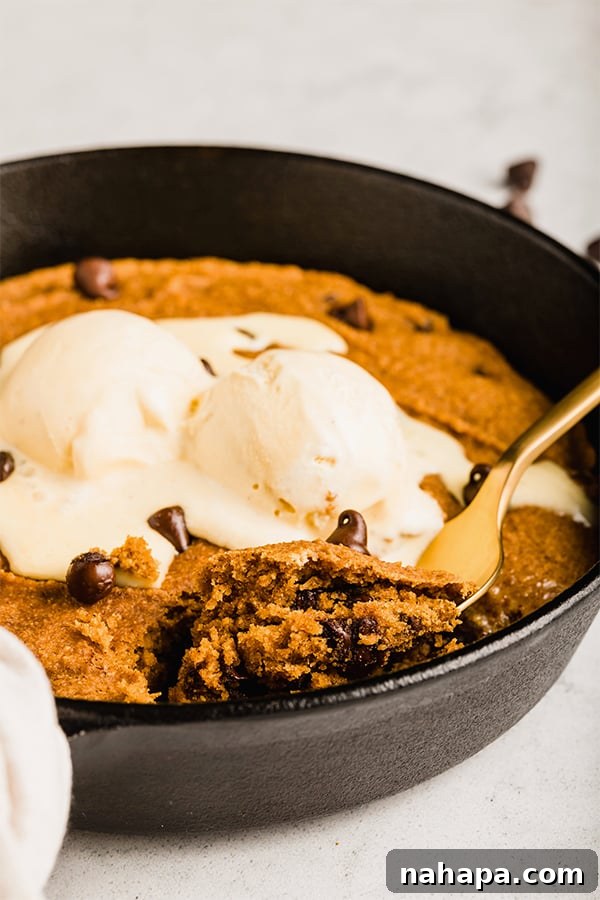 A close-up shot of the warm pumpkin chocolate chip cookie skillet, adorned with a melting scoop of coconut milk ice cream, highlighting its inviting texture.