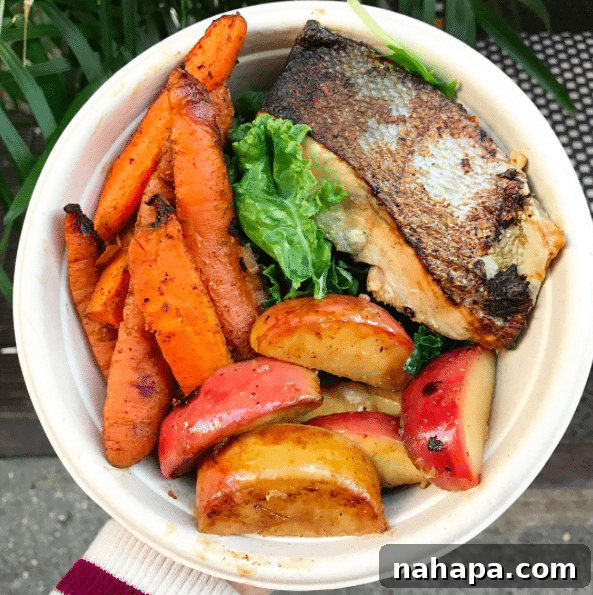 A vibrant bowl filled with salmon, crisp apples, fresh greens, and perfectly roasted carrots, ready to be enjoyed.