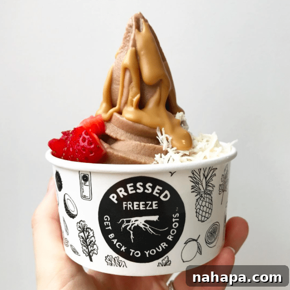 A cup from Pressed Juicery featuring a chocolate freeze topped with rich peanut butter drizzle, fresh strawberries, and shredded coconut.