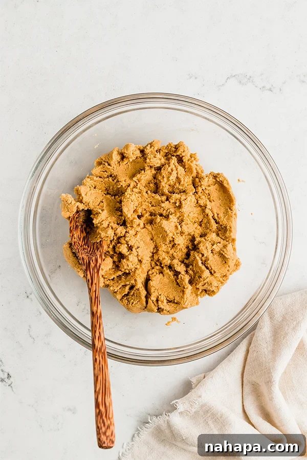 A bowl containing pumpkin pie donut hole batter, mixed to a thick consistency, with a wooden spoon resting inside.