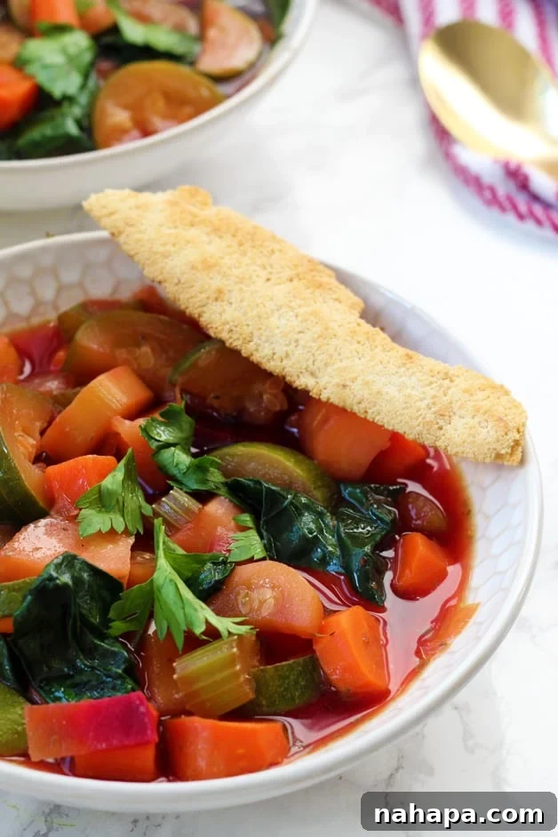 A bowl of minestrone soup with a cracker on it.