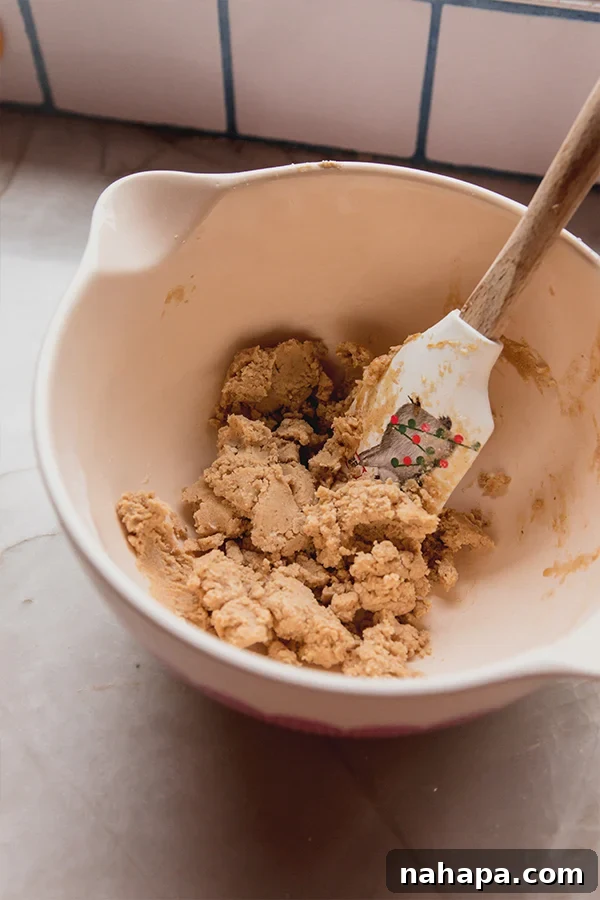 A bowl of spiced gingerbread donut holes dough being mixed by hand, showing its thick consistency.