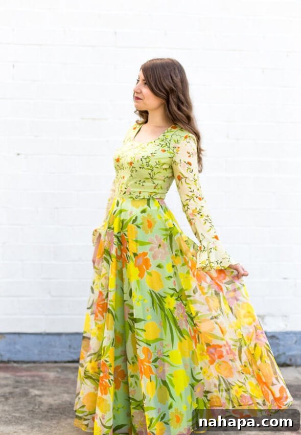 Michelle in a vibrant printed 1970s maxi dress against a white concrete background.
