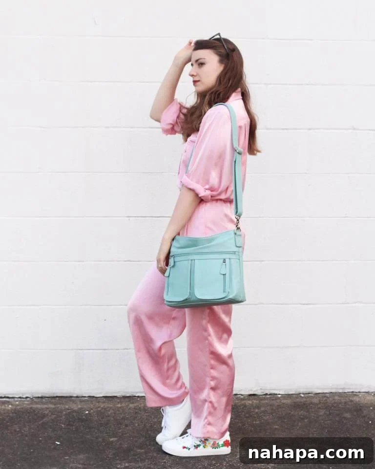 Michelle in a vibrant pink 80s jumpsuit, holding a blue purse against a white concrete background.