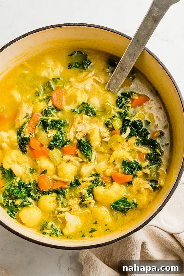 Vibrant yellow turmeric chicken soup in a bowl with fresh parsley garnish, ready to be enjoyed.