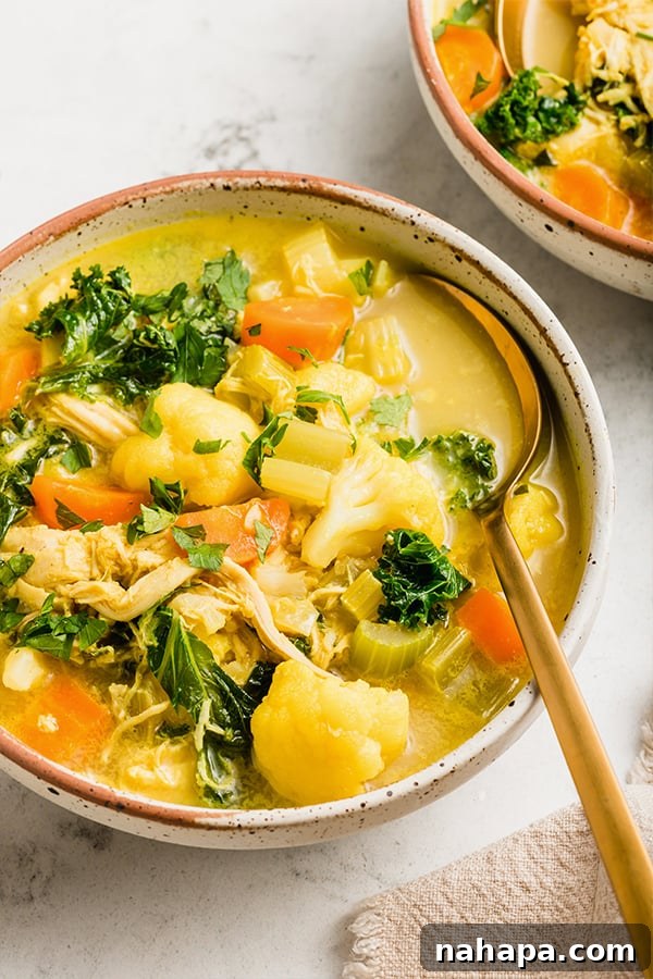 A close-up shot of the golden turmeric chicken soup with visible vegetables and chicken pieces, garnished with fresh herbs.