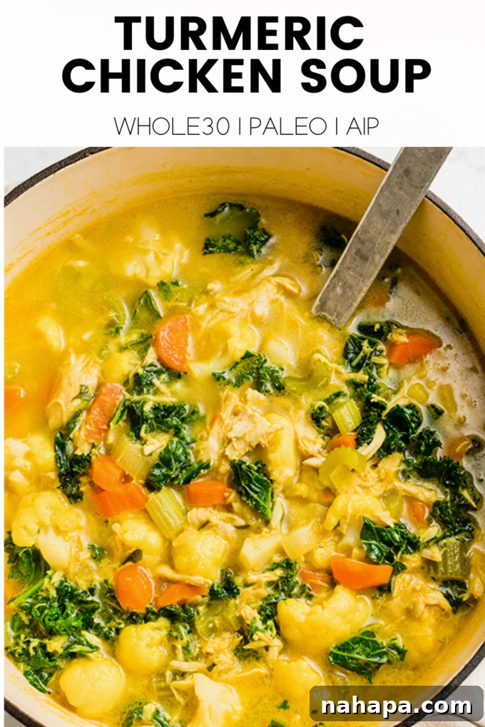 A bowl of rich turmeric chicken soup, garnished with fresh herbs and a slice of lemon on a textured background.