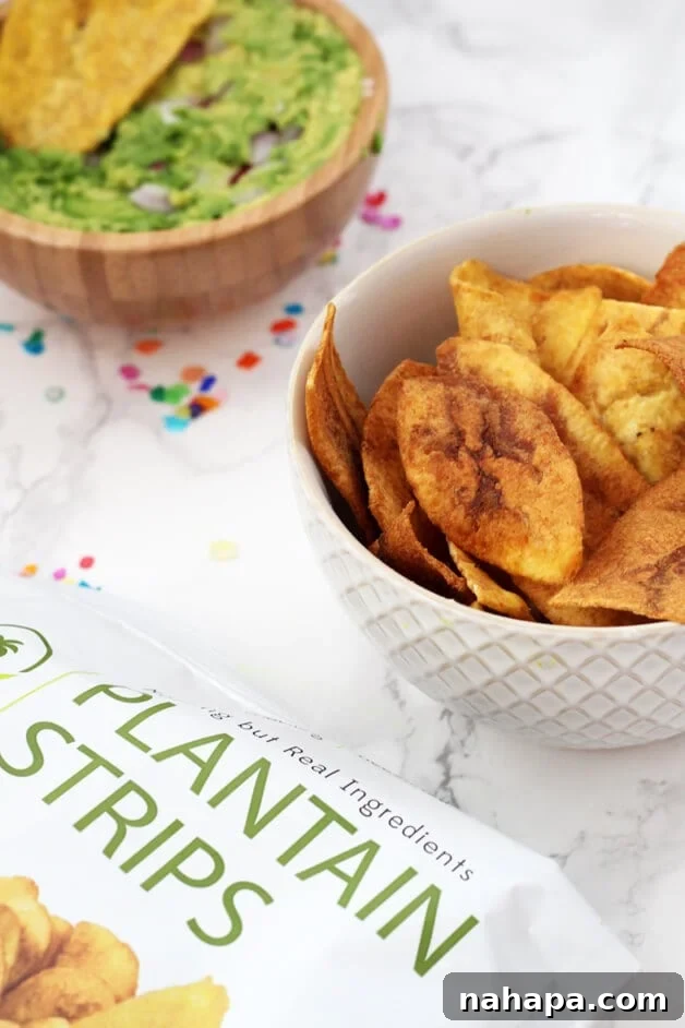 A white ceramic bowl brimming with golden-brown plantain strips, elegantly positioned beside a rustic wooden bowl filled with vibrant green guacamole.