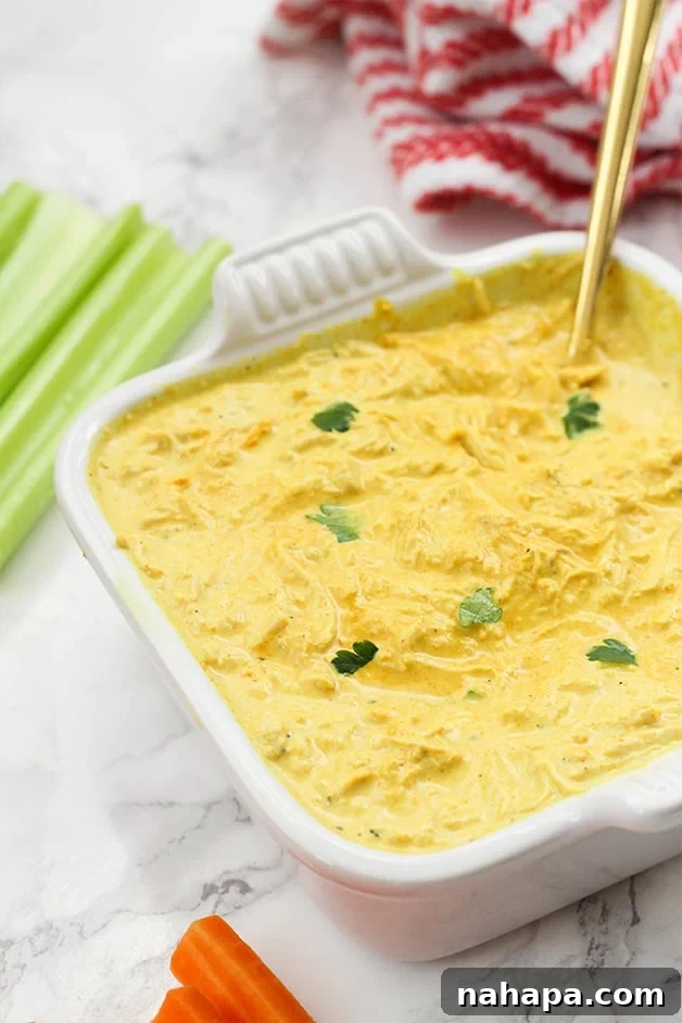 A white ceramic dish filled with buffalo chicken dip and a spoon in it and some celery next to it.
