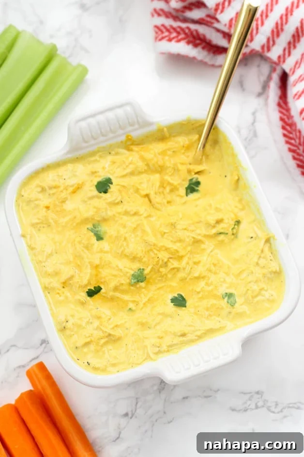 A white ceramic ceramic dish filled with buffalo chicken dip and a spoon in it and some celery next to it.