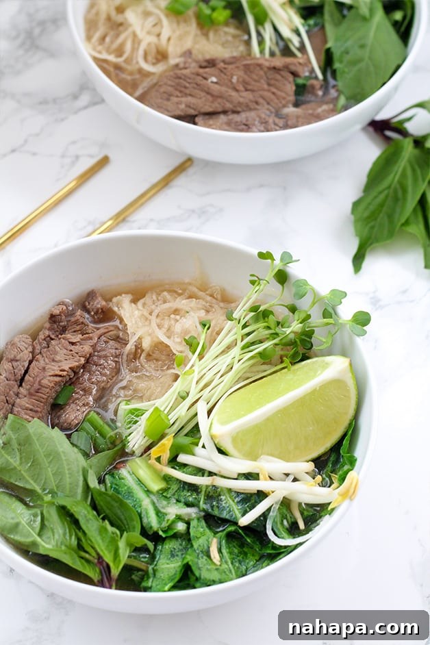 A close-up shot of a comforting bowl of Instant Pot Beef Pho, showcasing the rich broth, tender beef slices, spiralized daikon noodles, fresh green herbs, and a vibrant lime wedge, ready to be enjoyed with chopsticks.