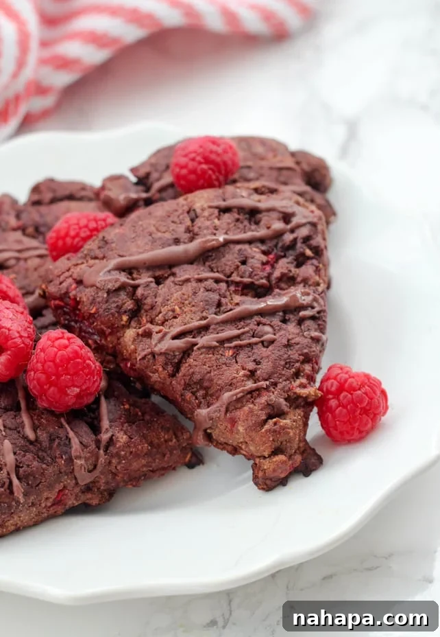 A white plate with paleo chocolate raspberry scones on it with fresh raspberries on top.