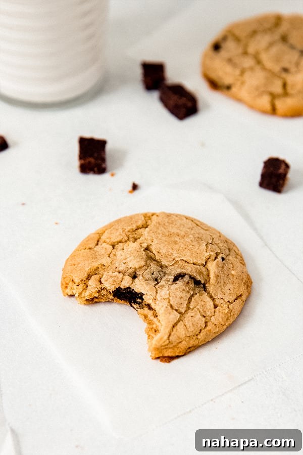 A paleo chocolate chip cookie with a bite taken out of it resting on a napkin, showcasing its soft interior.