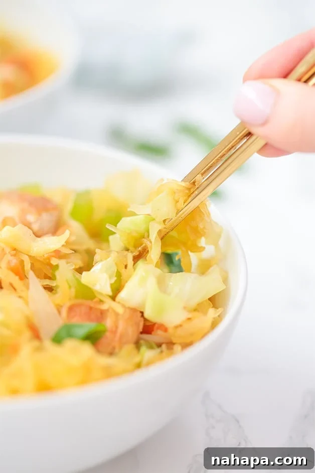 A white bowl filled with chow mein and a hand with gold chop sticks in it.