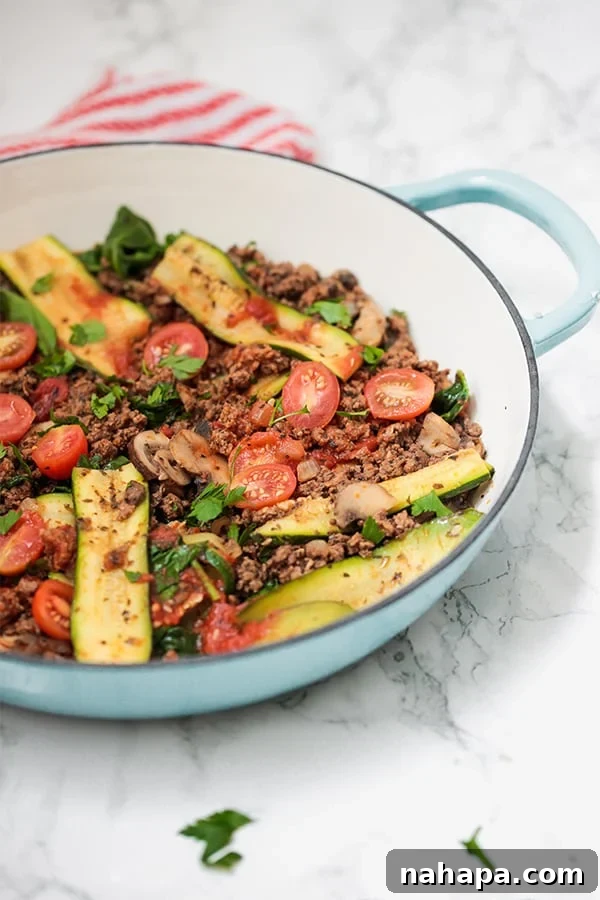 A blue pan filled with zucchini, ground beef, and herbs, resembling a deconstructed lasagna.