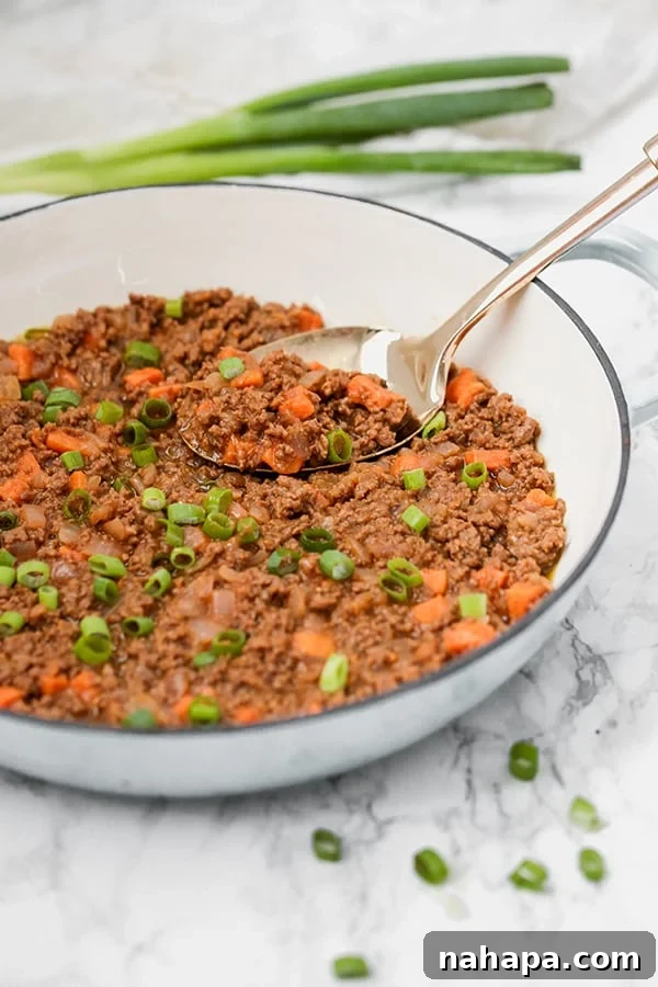 A white skillet filled with sloppy joes and a large metal serving spoon.