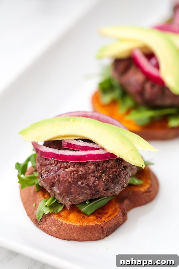 A slider on a sweet potato bun topped with red onion and avocado, with another in the background.
