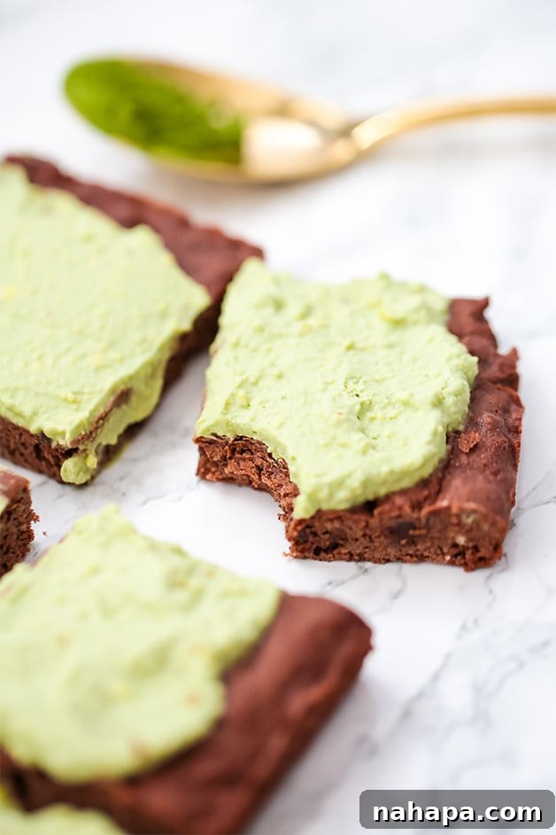 A few matcha brownies on a counter with a bite taken out of one of them, showcasing the green frosting.
