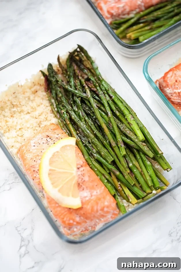 Healthy Paleo AIP Whole30 Salmon Meal Prep Bowls 2 A glass meal prep container filled with roasted asparagus, salmon, and cauliflower rice, ready for a healthy meal.