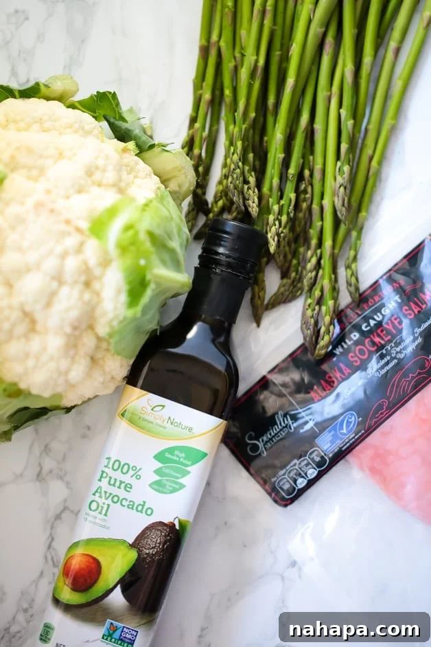 Healthy Paleo AIP Whole30 Salmon Meal Prep Bowls 3 Avocado oil, a head of cauliflower, fresh asparagus, and raw salmon fillets laid out on a kitchen counter before cooking.