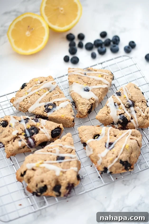 Six lemon blueberry scones on a metal cooling rack with fresh blueberries and lemon slices nearby.