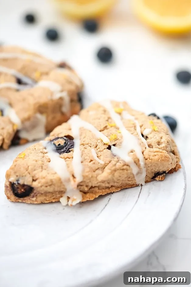 A white plate with two lemon blueberry scones with frosting on it.