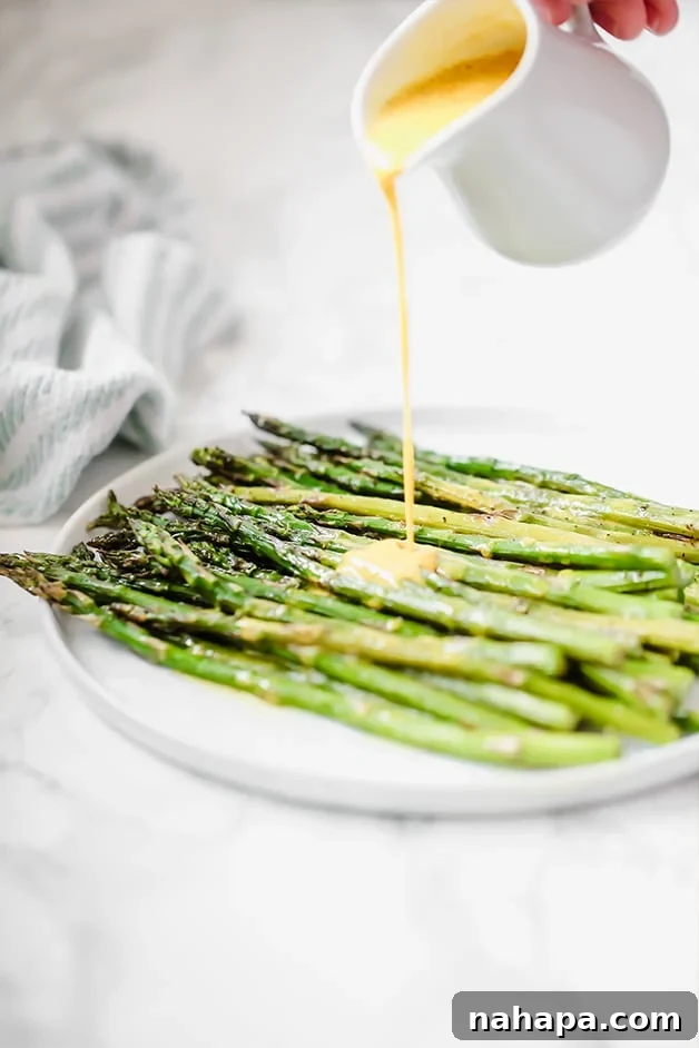 A white plate filled with roasted asparagus, drizzled generously with a golden turmeric sauce.