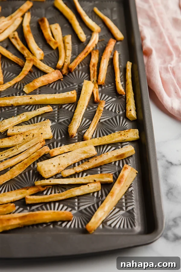 Crispy baked parsnip fries spread out on a parchment-lined baking sheet, golden brown and fresh from the oven.