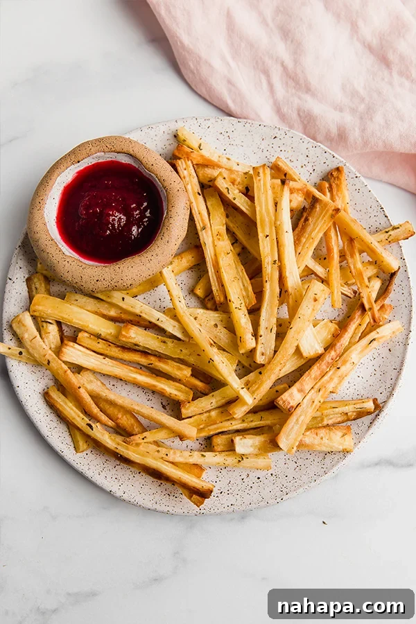 A close-up shot of crispy baked parsnip fries artfully arranged on a plate with a dollop of creamy dipping sauce on the side.