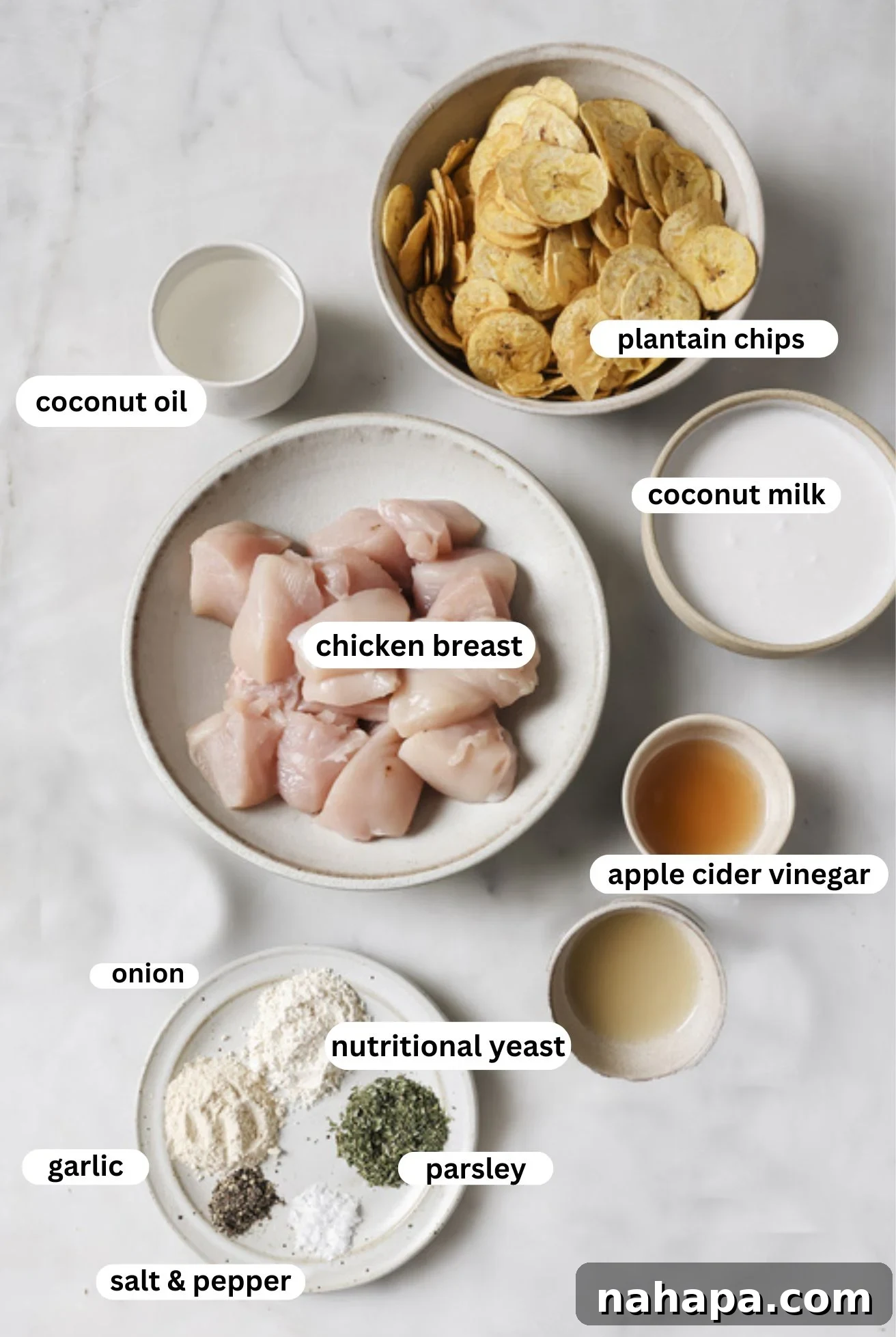 A selection of crispy chicken nugget ingredients arranged in small bowls, including chicken breast, plantain chips, coconut oil, coconut milk, apple cider vinegar, and various seasonings.