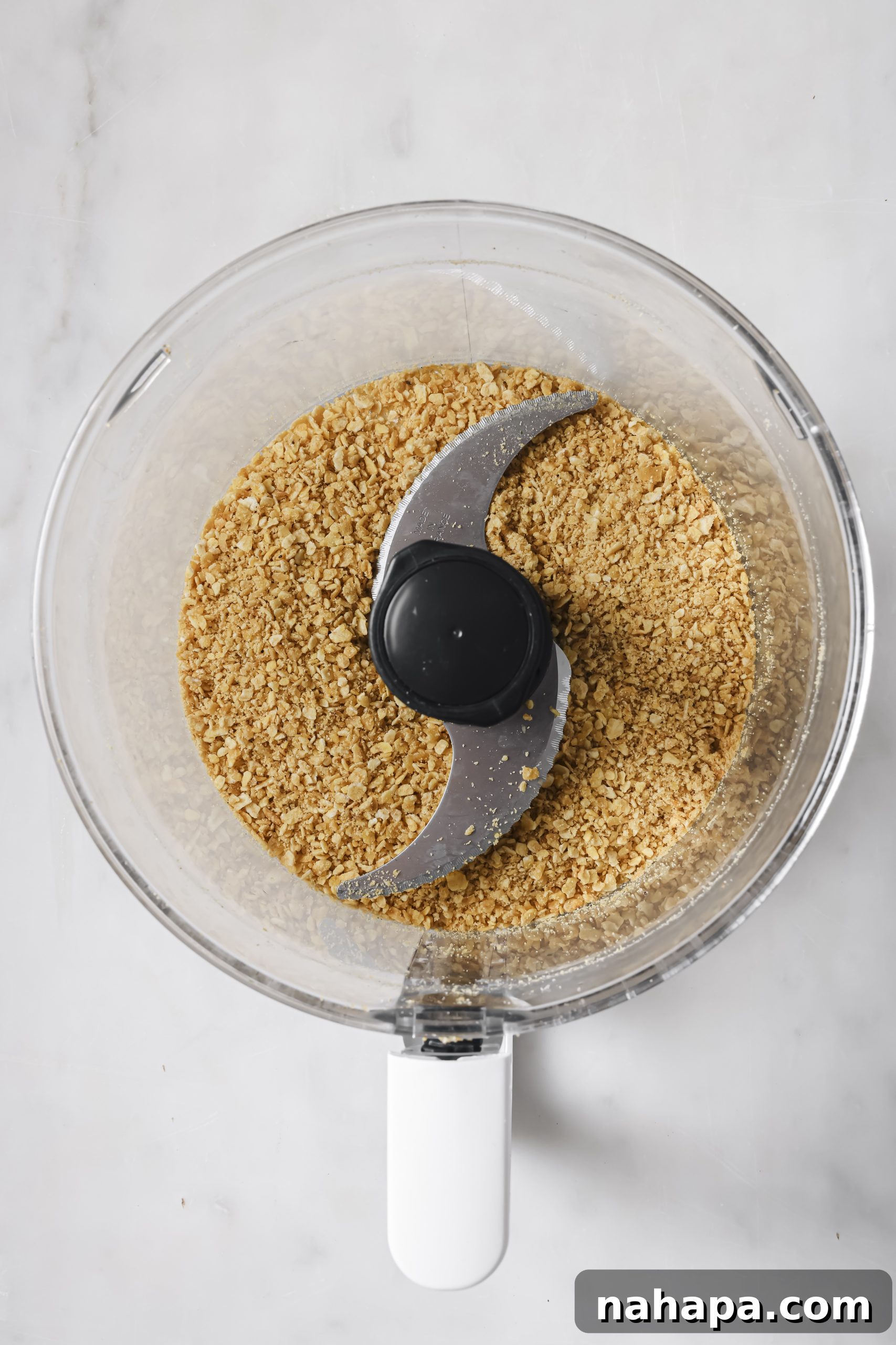 Plantain chips being finely ground in a food processor, creating a breading-like consistency.