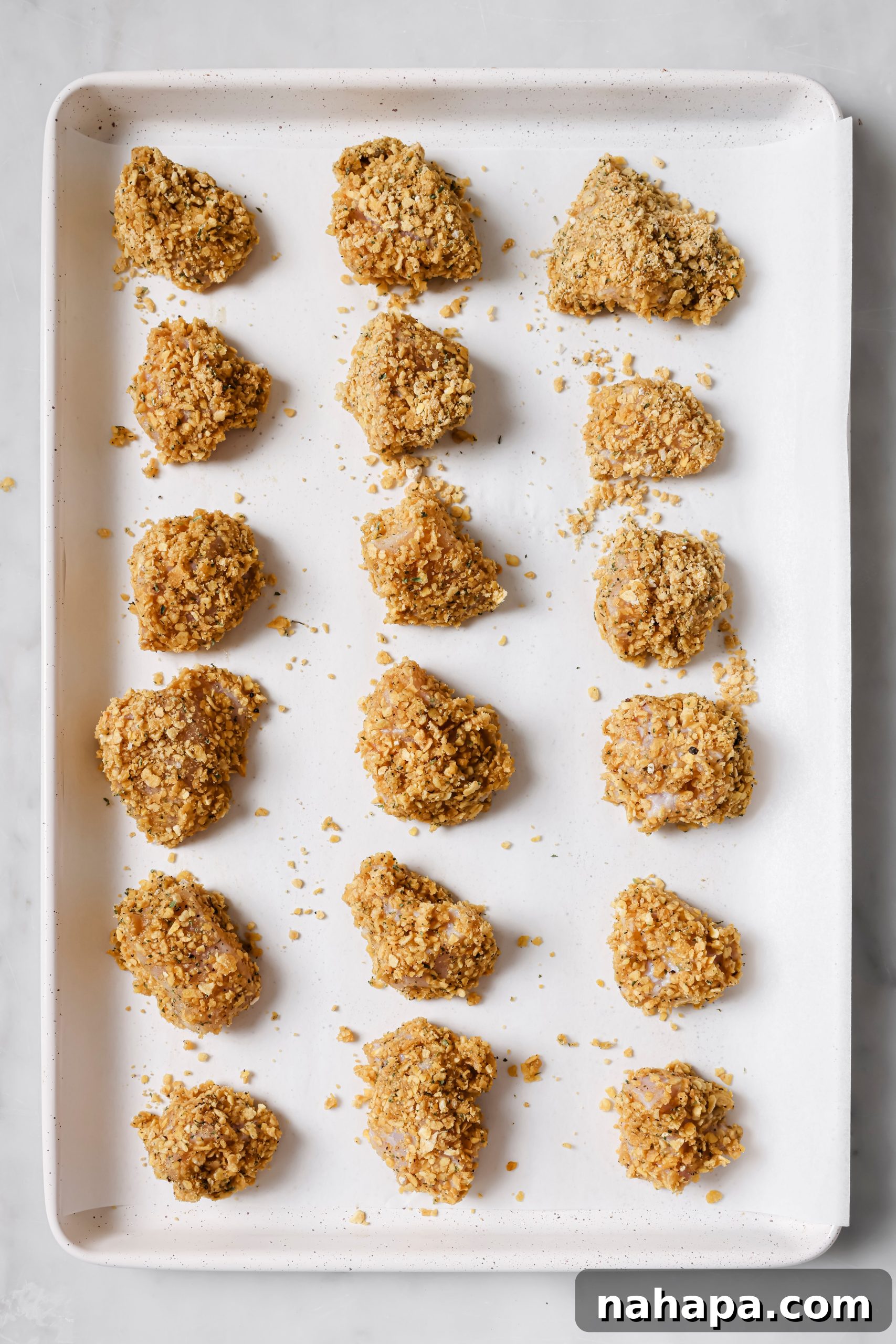Coated chicken nuggets neatly arranged on a parchment-lined baking sheet, ready for baking.
